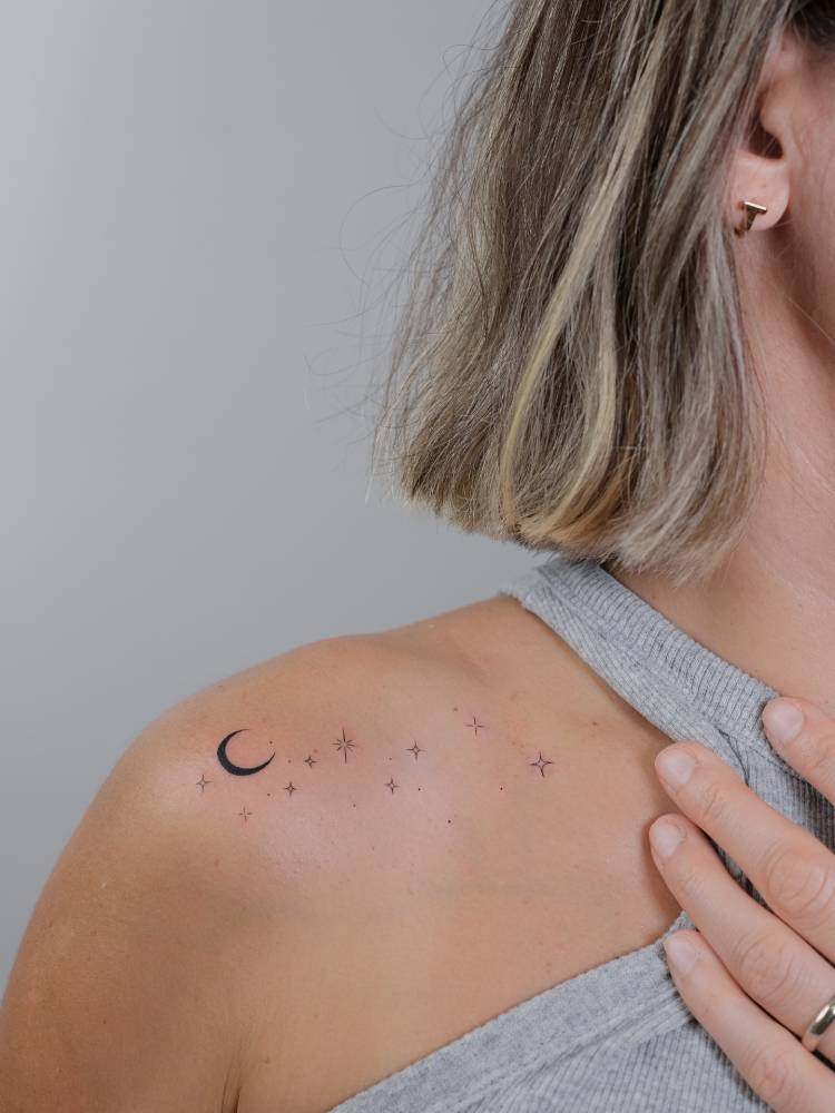 Minimalist crescent moon and sparkling stars tattoo placed on the shoulder.