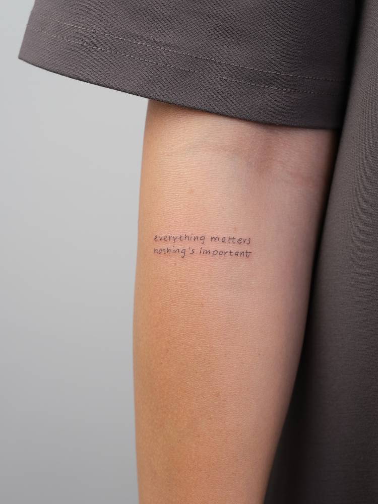 "Everything matters, nothing's important" lettering tattoo located on the inner forearm.