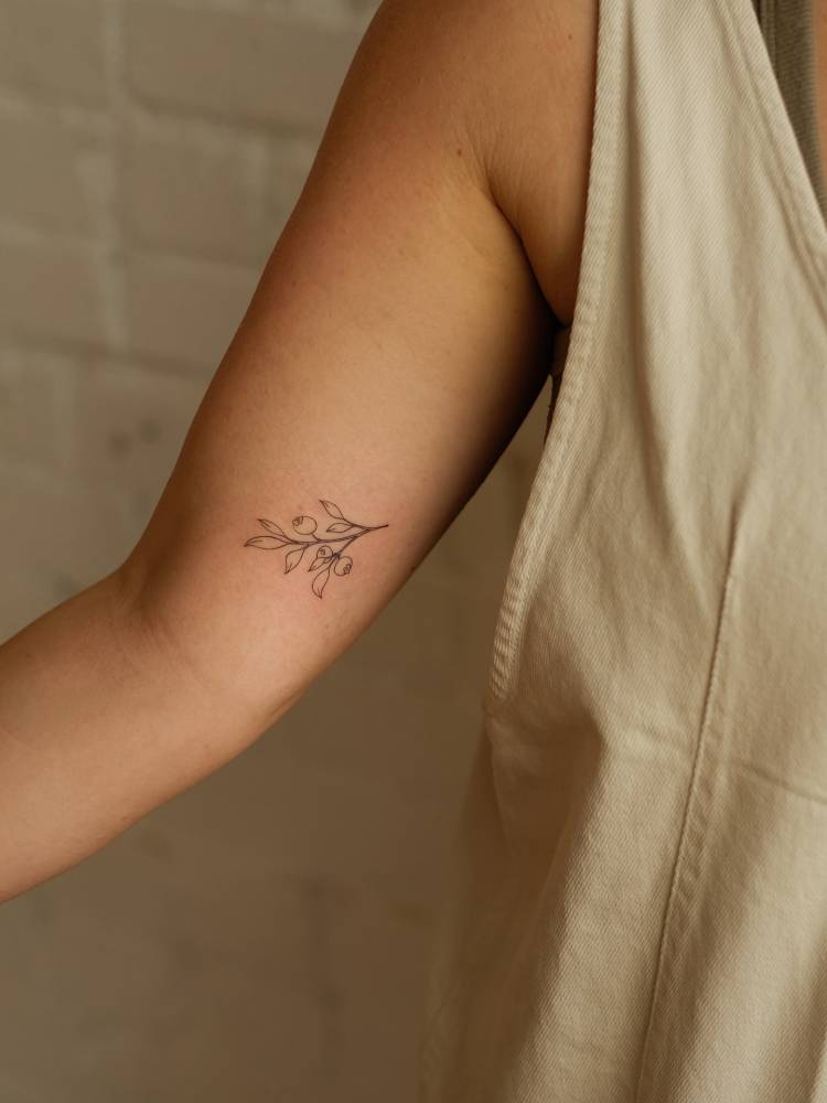 Olive branch tattoo located on the inner arm, done in fine line style.