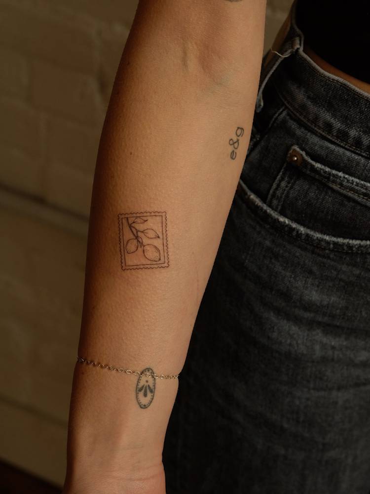 Lemon stamp tattoo placed on the inner forearm, fine line style.