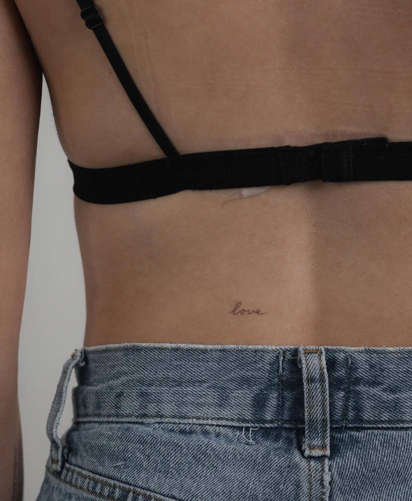 Tiny lettering tattoo of the word "love" located on the lower back.