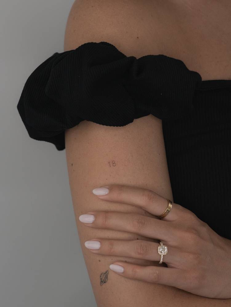 Little minimalistic tattoo of the number "18" located on the upper arm.