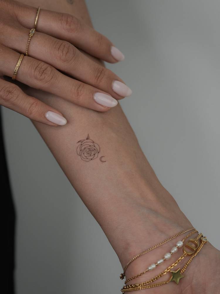 Rose head tattoo in fine line style located on the wrist.