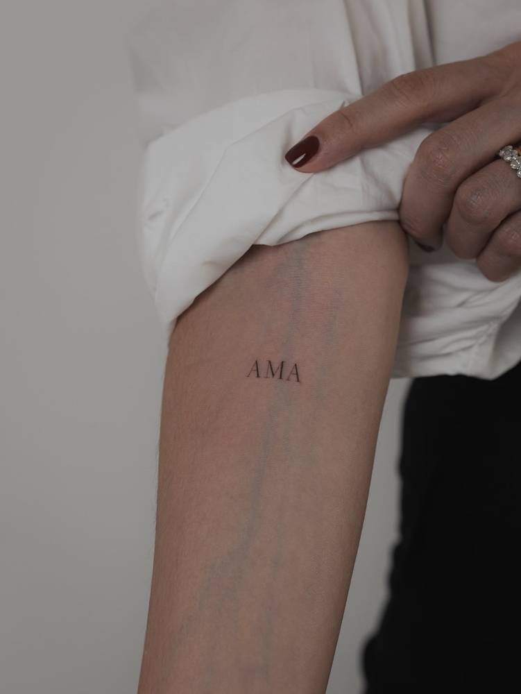 Word "ama" in serif font tattooed on the inner forearm.