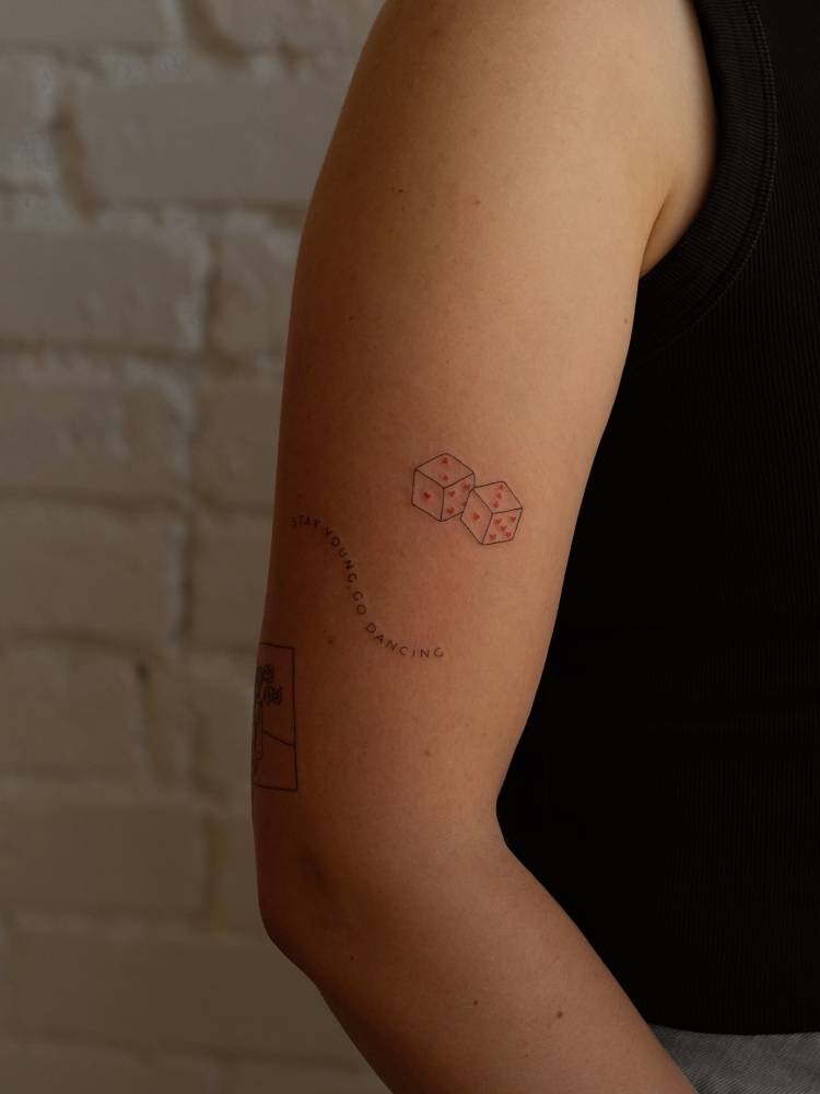 Fine line style little dice tattooed on the upper arm.