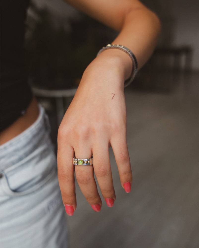 Tiny minimalistic tattoo of the number "7" located on the hand.