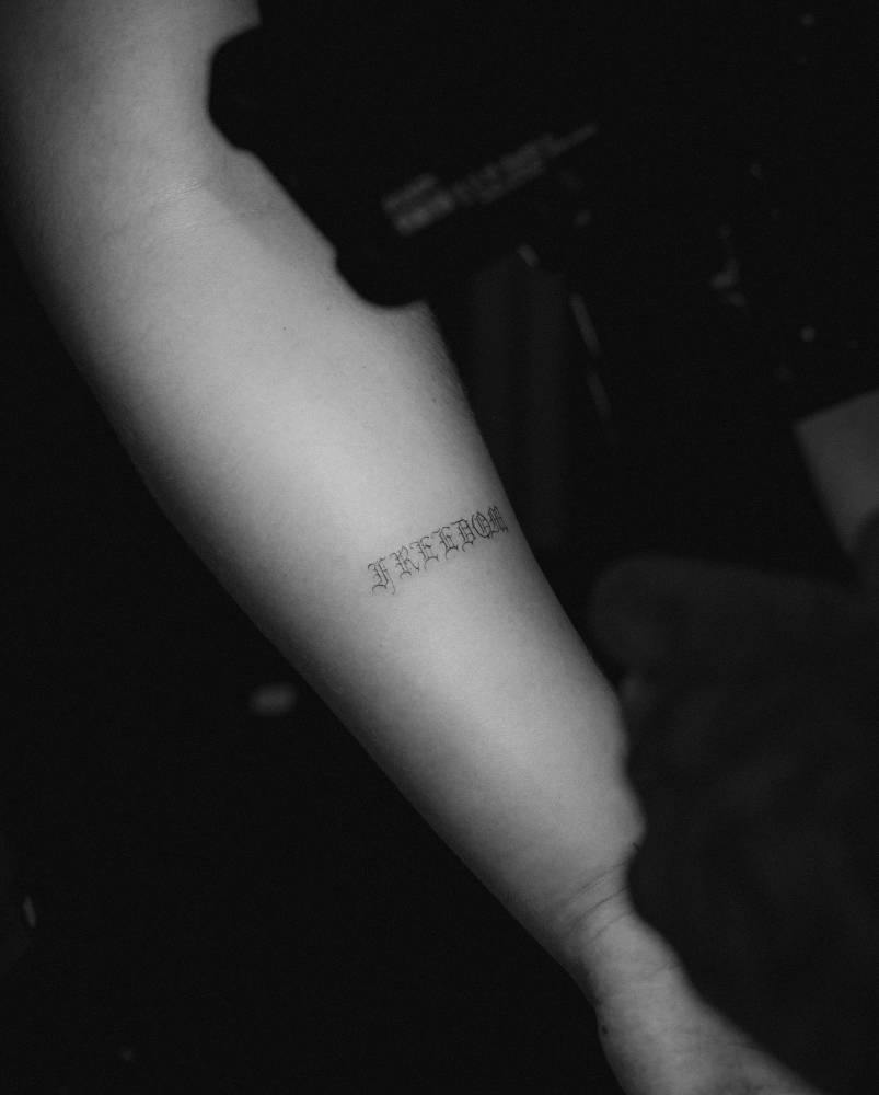 Word "freedom" in gothic font tattooed on the inner forearm.