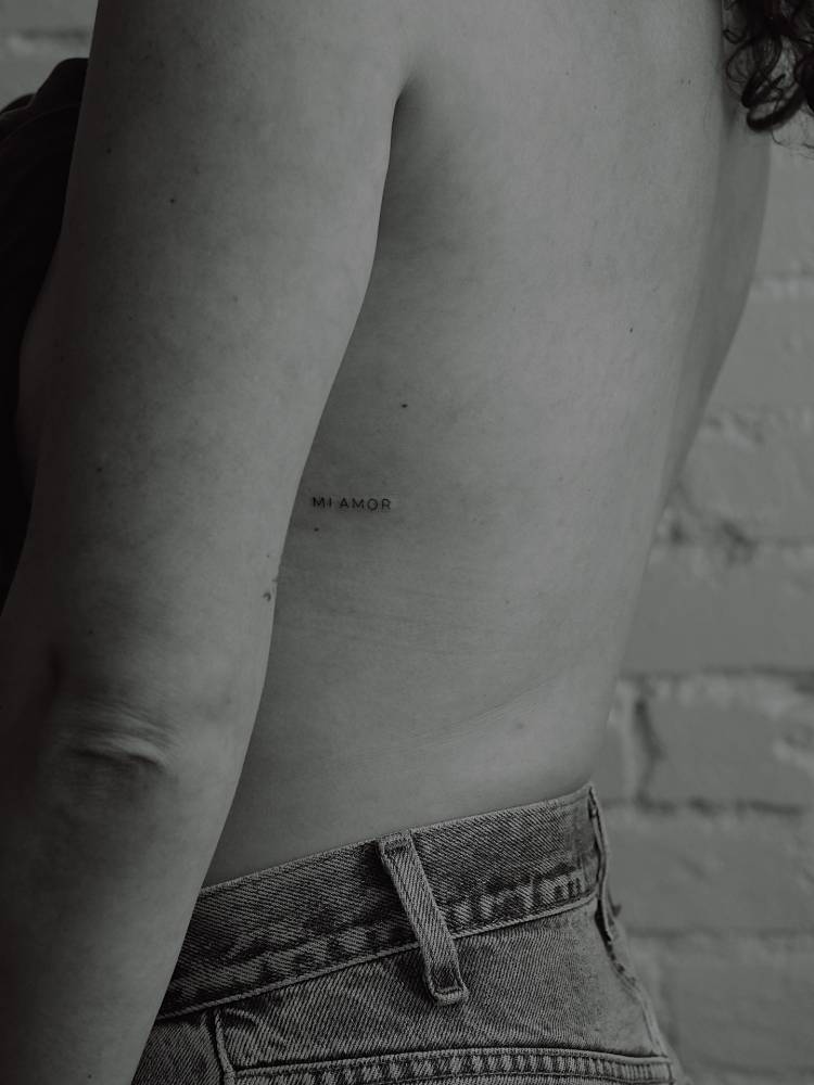 Lettering tattoo that says "mi amor" located on the rib.