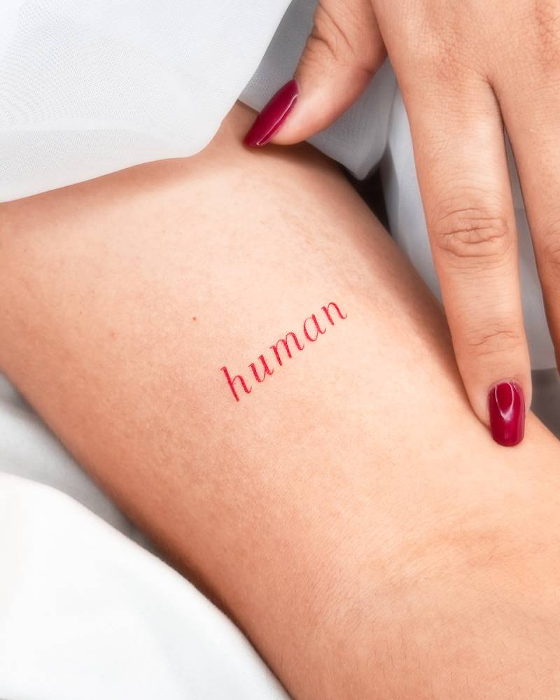 Word "human" in red ink tattooed on the bicep.
