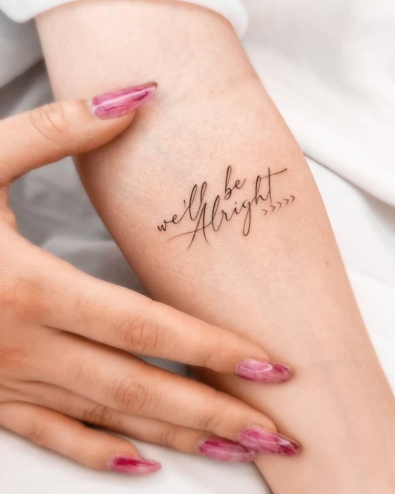 "We'll be alright" lettering tattoo located on the inner forearm.