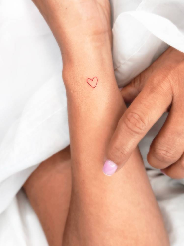 Tiny minimalistic red heart tattoo located on the wrist.