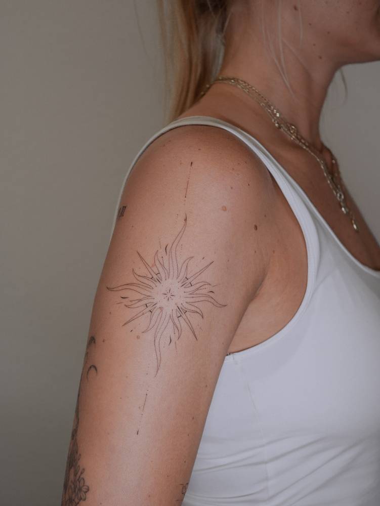 Sun tattoo in fine line style located on the upper arm.