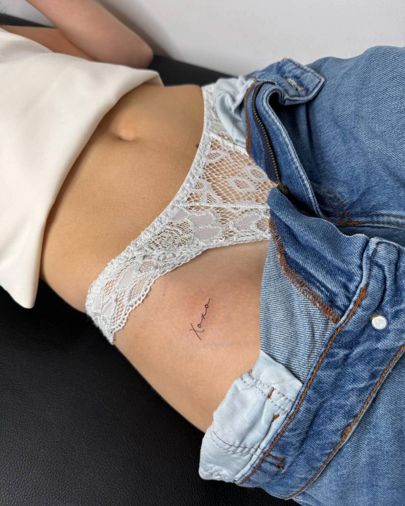 Handwritten font "xoxo" lettering tattoo placed on the pelvis.