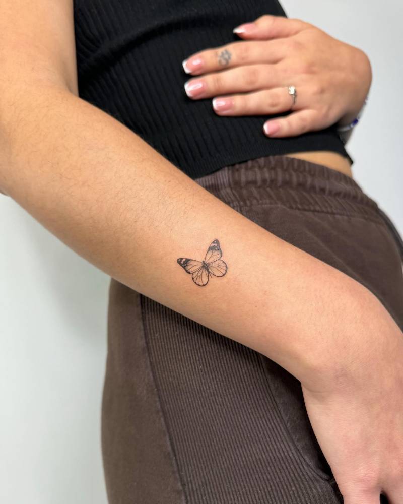 Little butterfly tattoo in illustrative style located on the wrist.
