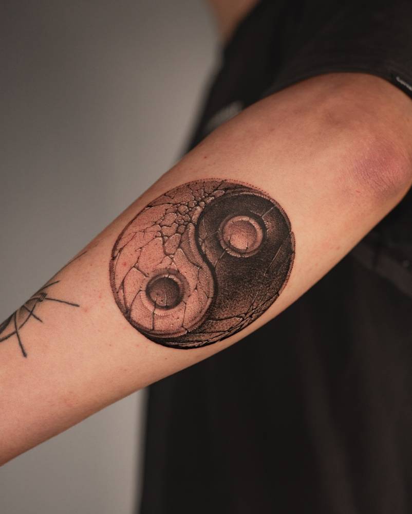 Yin Yang tattoo in black and grey style located on the forearm.