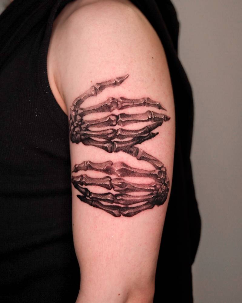 Skeleton hands tattoo in black and grey style located on the upper arm.