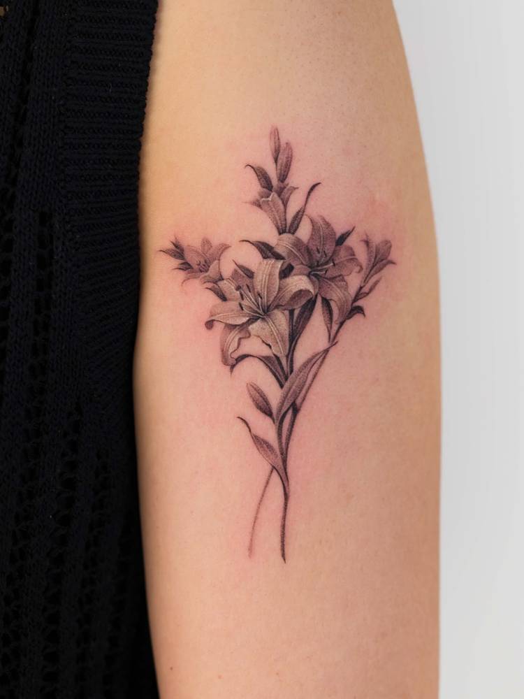 Lily bouquet tattoo in micro-realistic style located on the upper arm.