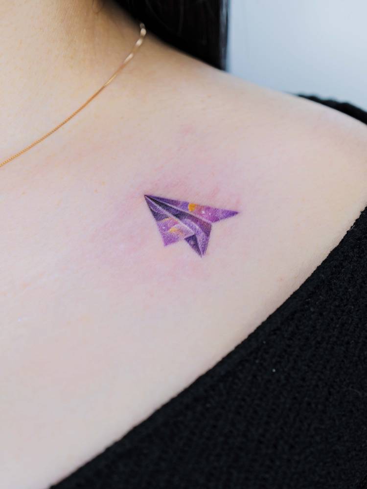 Watercolor style paper plane tattoo done on the collarbone.