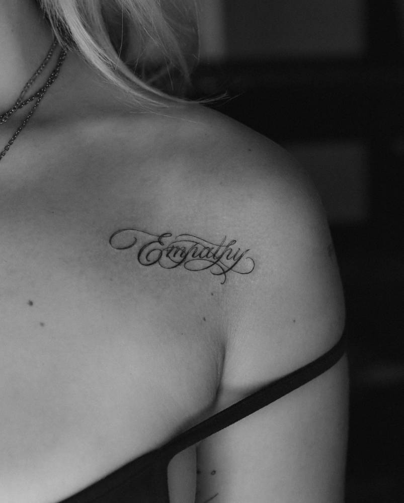 Lettering tattoo of the word "empathy" located on the shoulder.