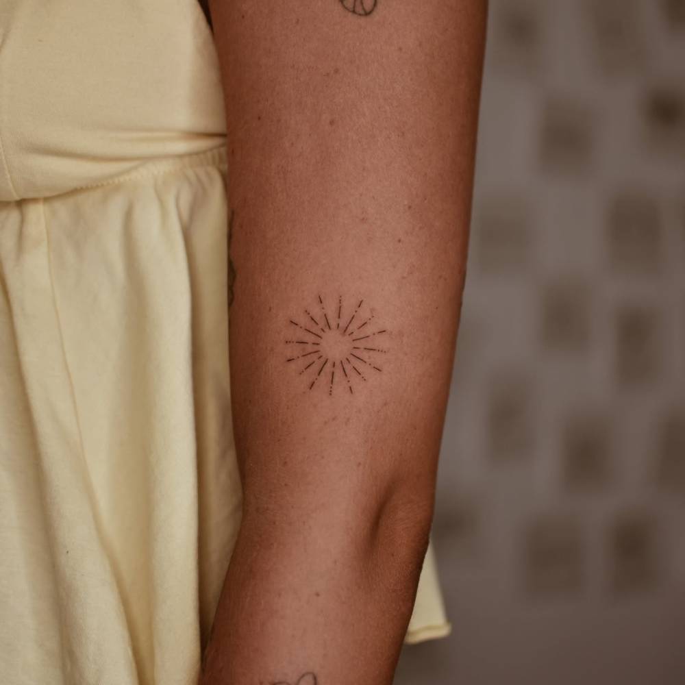 Little sun tattoo in fine line style done on the upper arm.