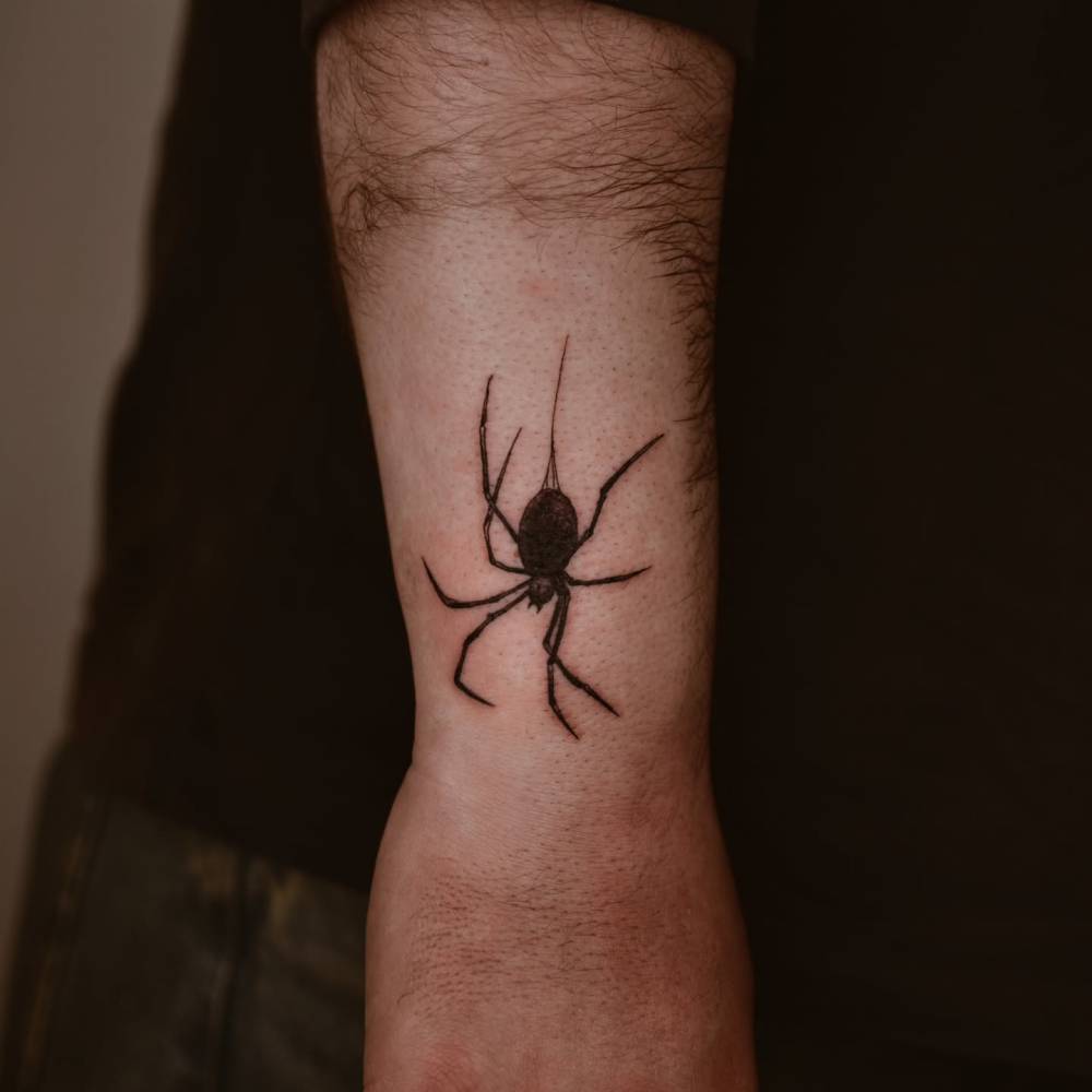 Blackwork style spider tattoo located on the wrist.