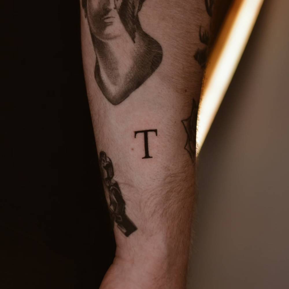 Little letter "T" tattoo in serif font placed on the wrist.