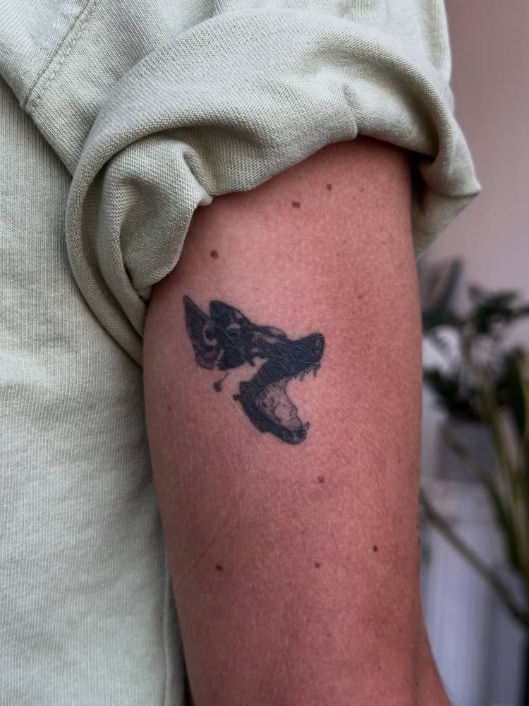 Wolf head tattoo in blackwork style located on the tricep.