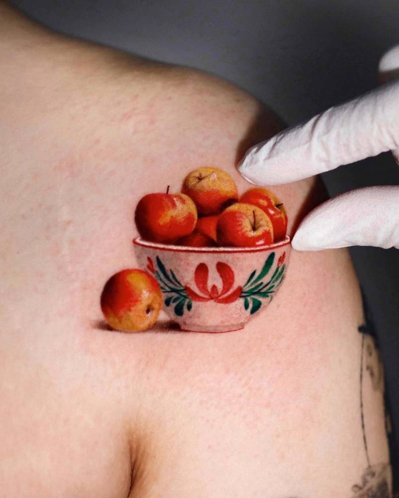 Micro-realistic style apple bowl tattoo located on the shoulder.