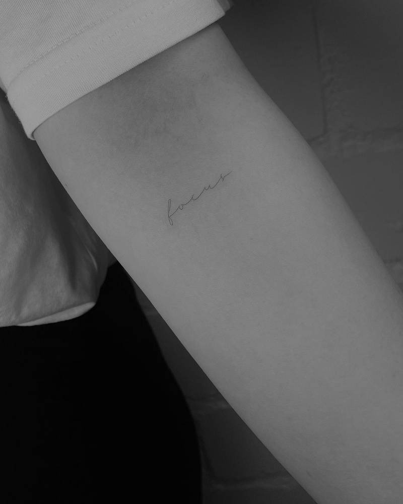 Tattoo of the word "focus" handwritten on the inner forearm.