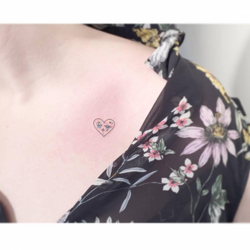 Universe in a heart tattoo located on the collarbone, done in minimalistic style.