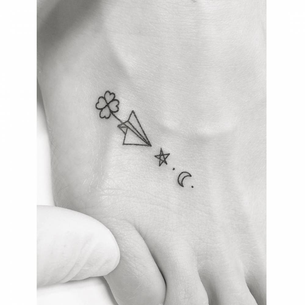 Clover, paper plane, star and moon tattooed on the foot, minimalistic style.