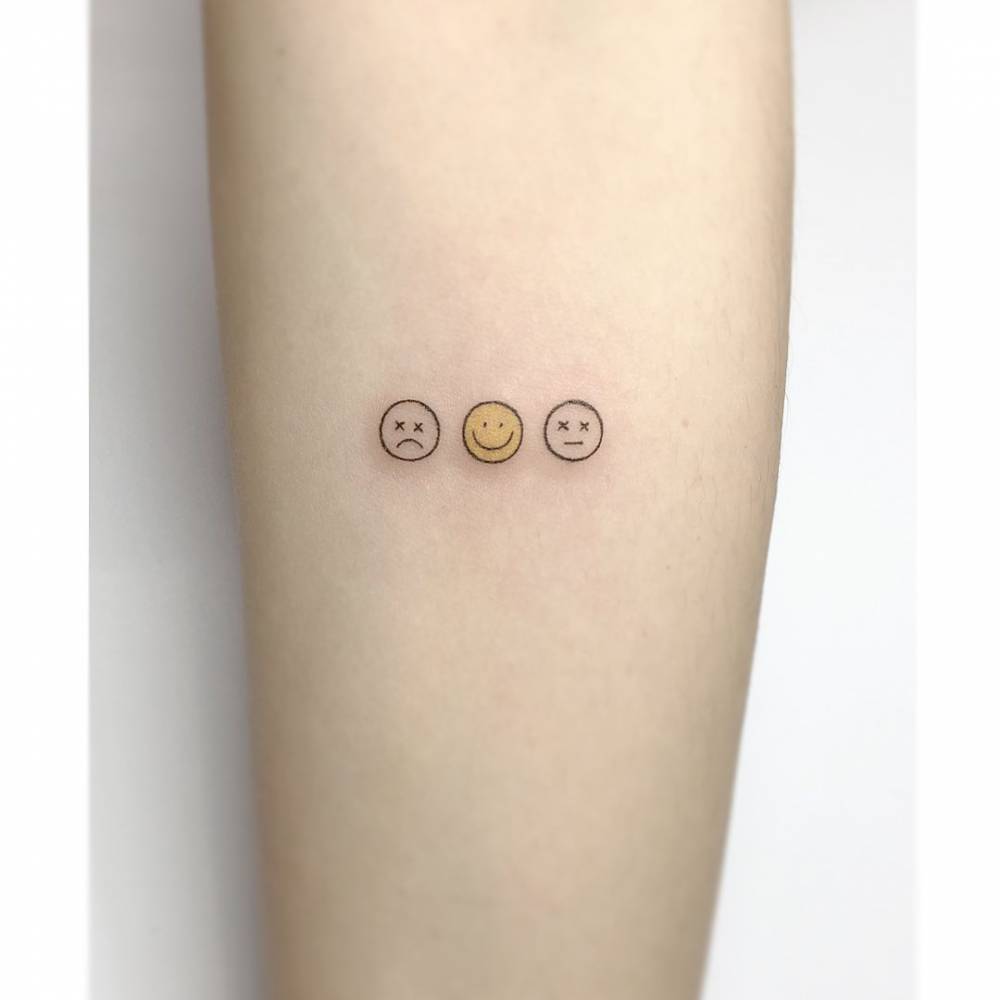 Sad face and smiley tattooed on the inner forearm, minimalistic style.