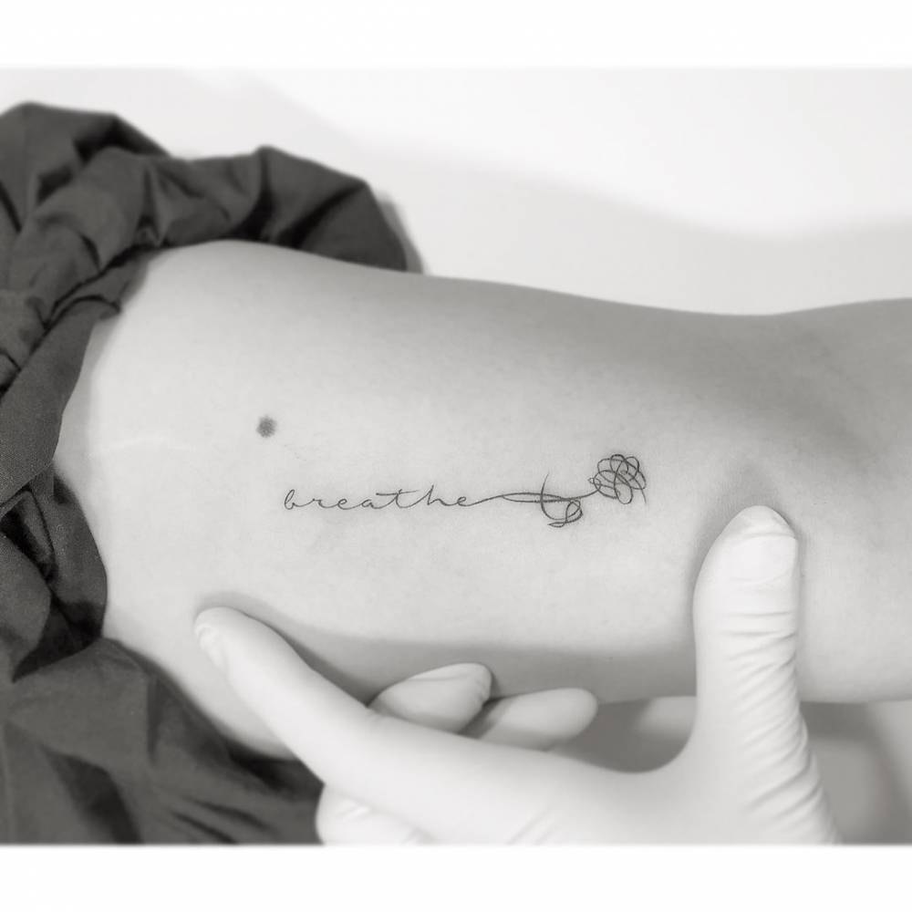 Word "breathe" and flower tattooed on the inner arm.