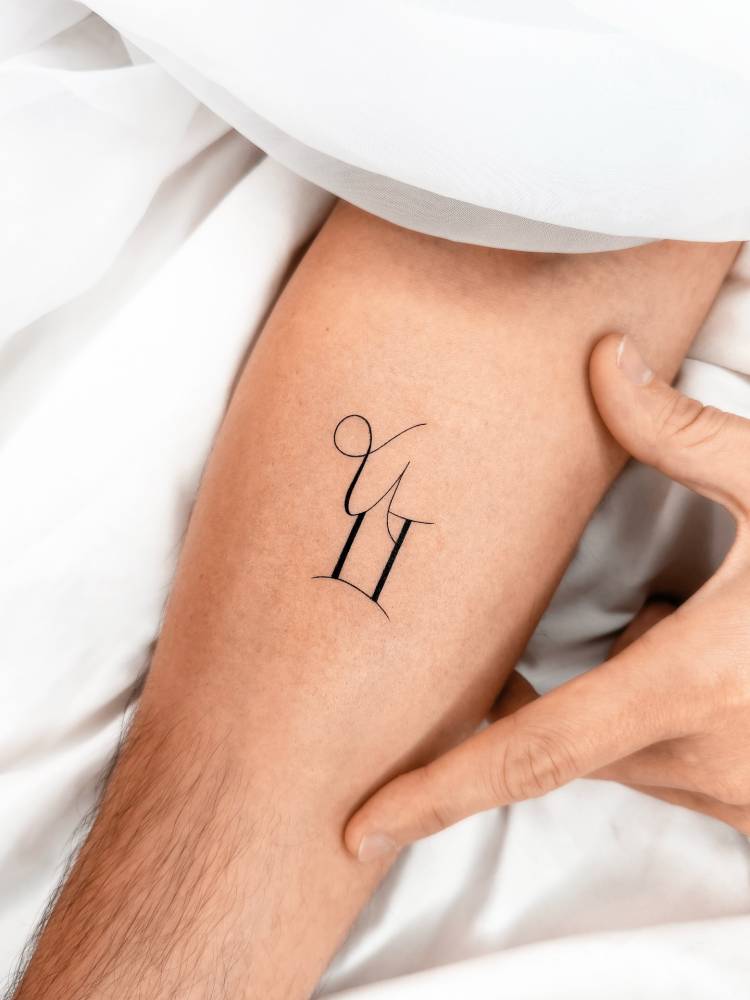 Capricorn and Gemini zodiac symbols tattooed on the inner forearm.