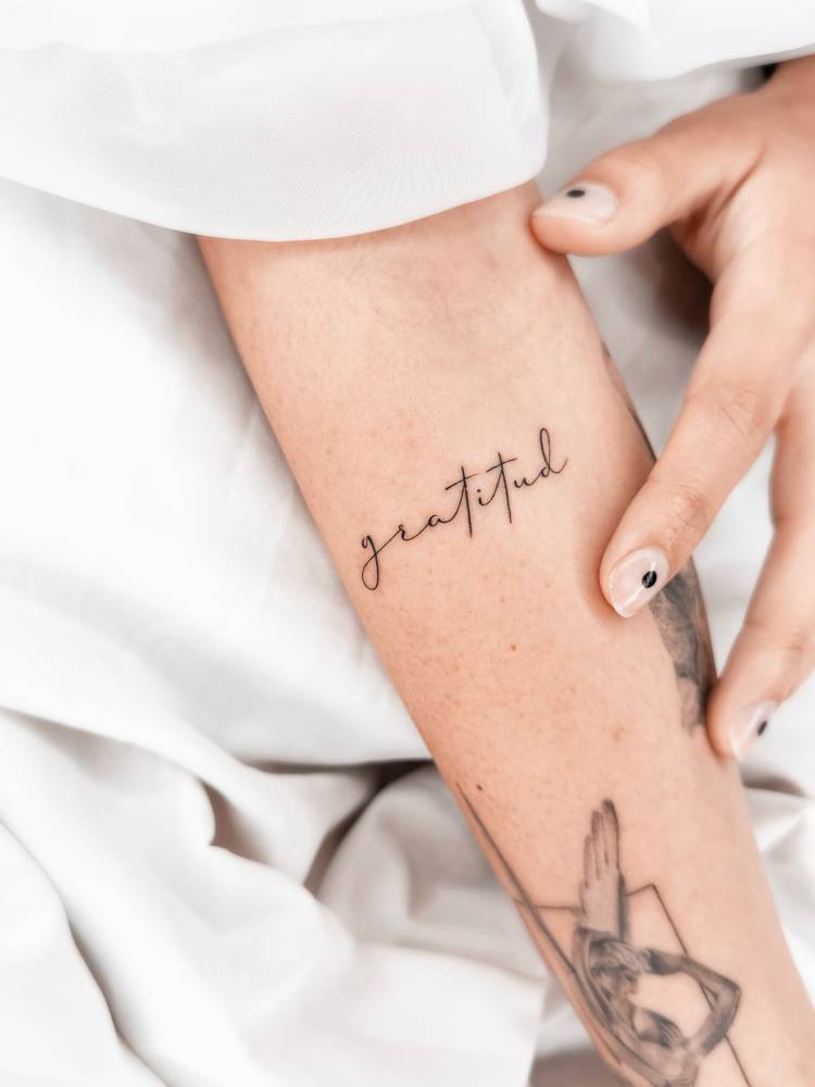 Handwritten font word "gratitud" tattoo located on the inner forearm.