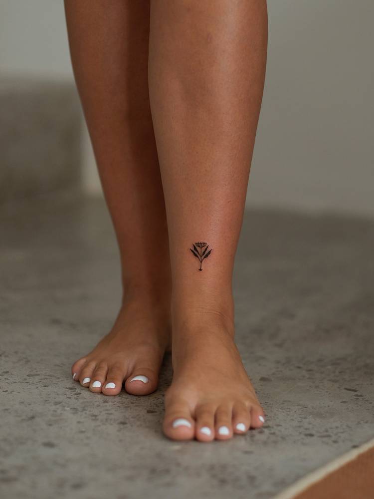 Little flower tattoo in blackwork style located on the ankle.