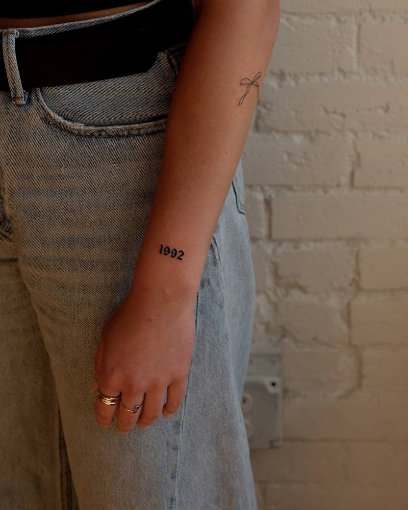"1992" birth year in gothic font tattooed on the wrist.