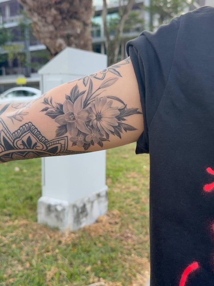 Healed narcissus and daisy flowers tattooed on the inner arm, black and grey style.
