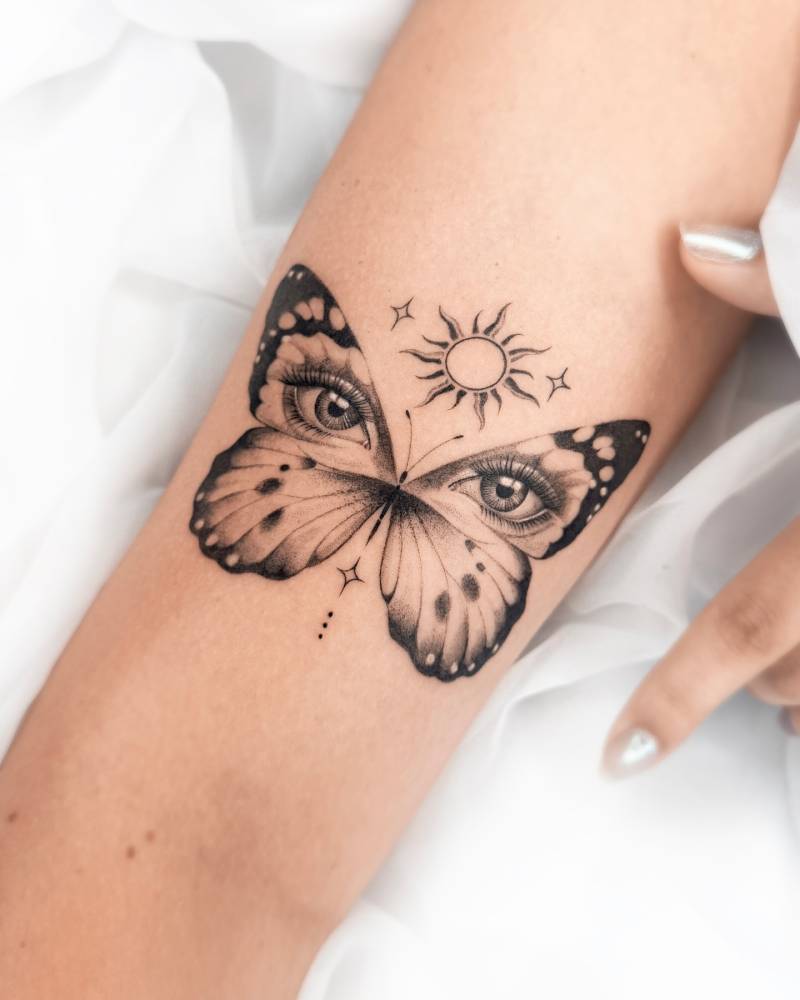 Butterflies and eyes tattoo in illustrative style located on the inner forearm.