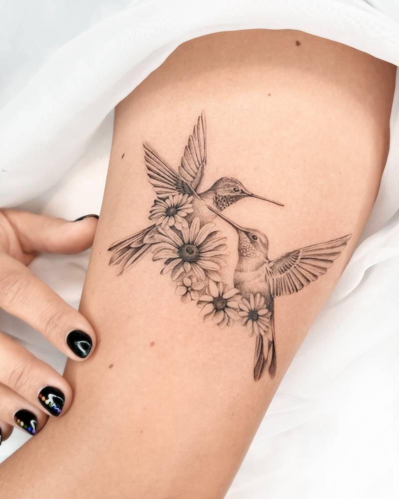 Micro-realistic style hummingbirds and daisies tattooed on the upper arm.
