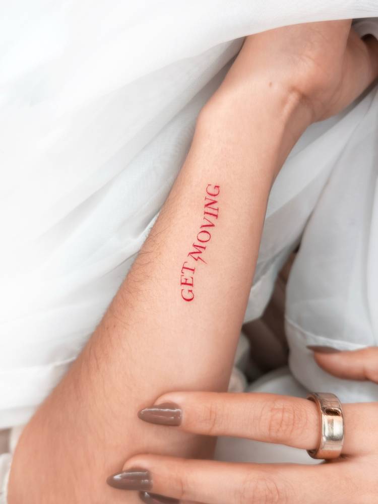 "Get moving" lettering tattoo in red ink placed on the wrist.