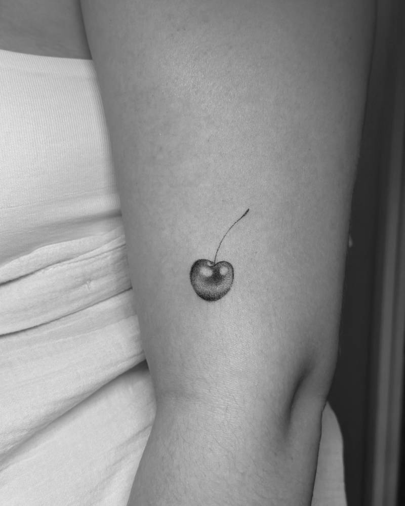 Micro-realistic style cherry tattoo located on the upper arm.