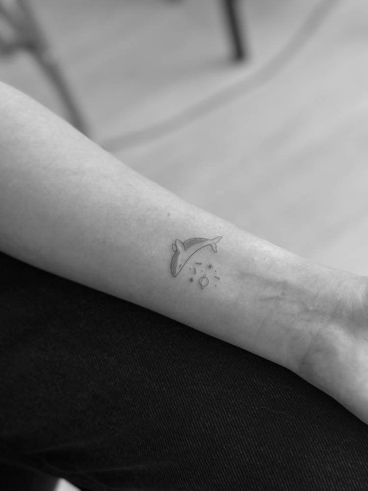 Whale and universe tattoo in minimalistic style located on the wrist.