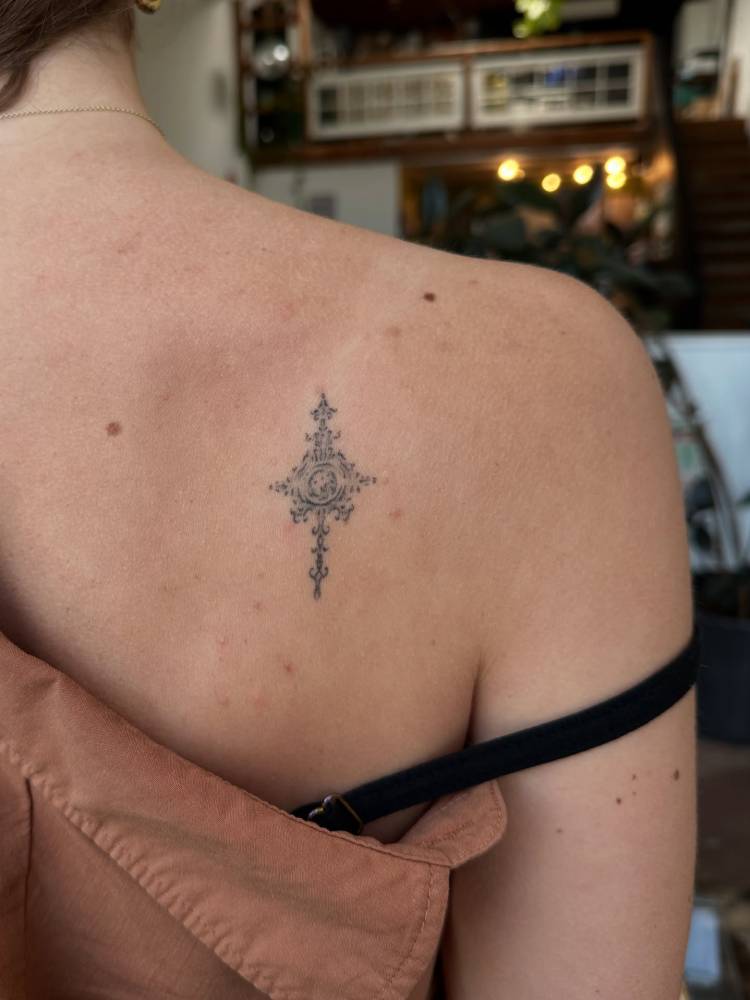 Healed ornamental tattoo located on the shoulder blade.