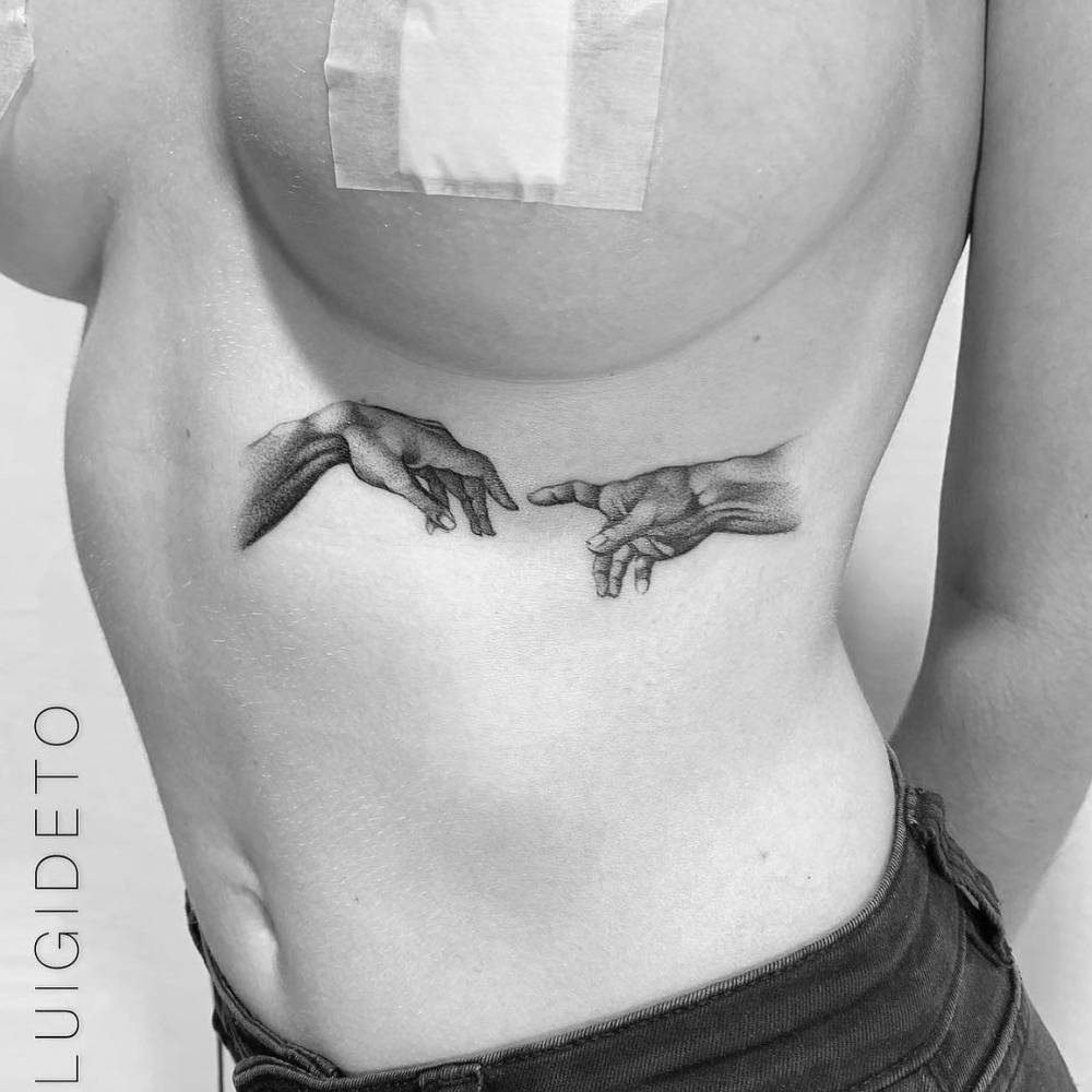 Blackwork style 'Creation of Adam' hands tattoo located on the rib.
