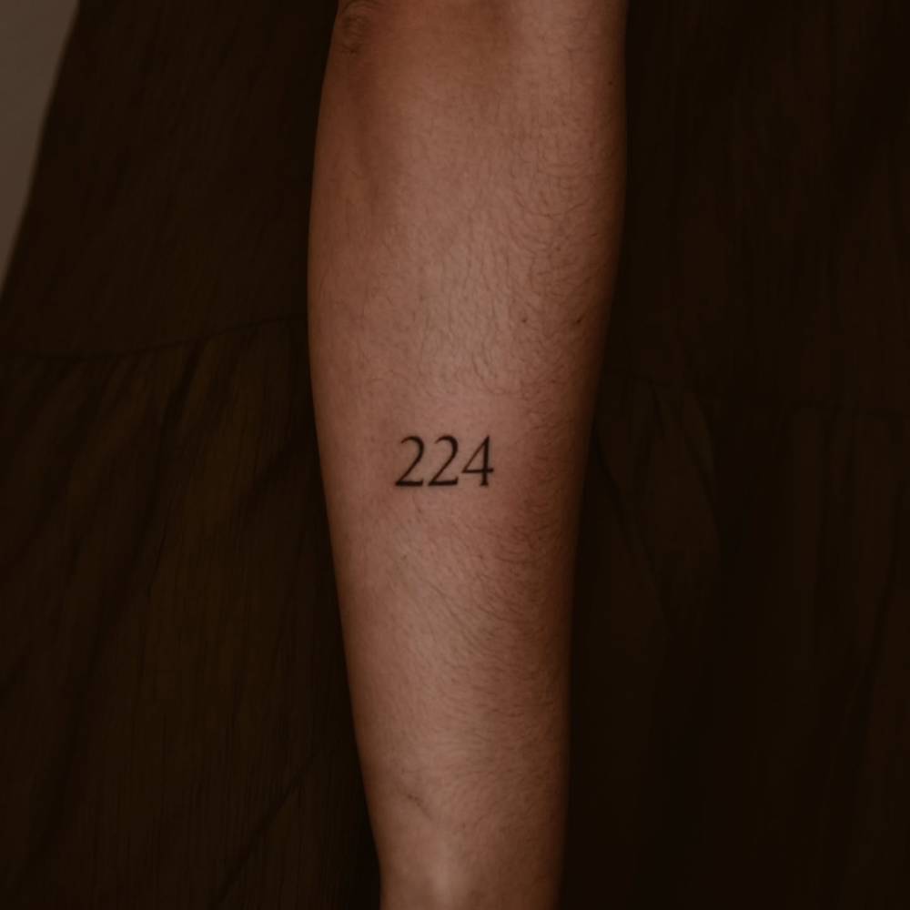 Lettering tattoo of the number "224" located on the forearm.