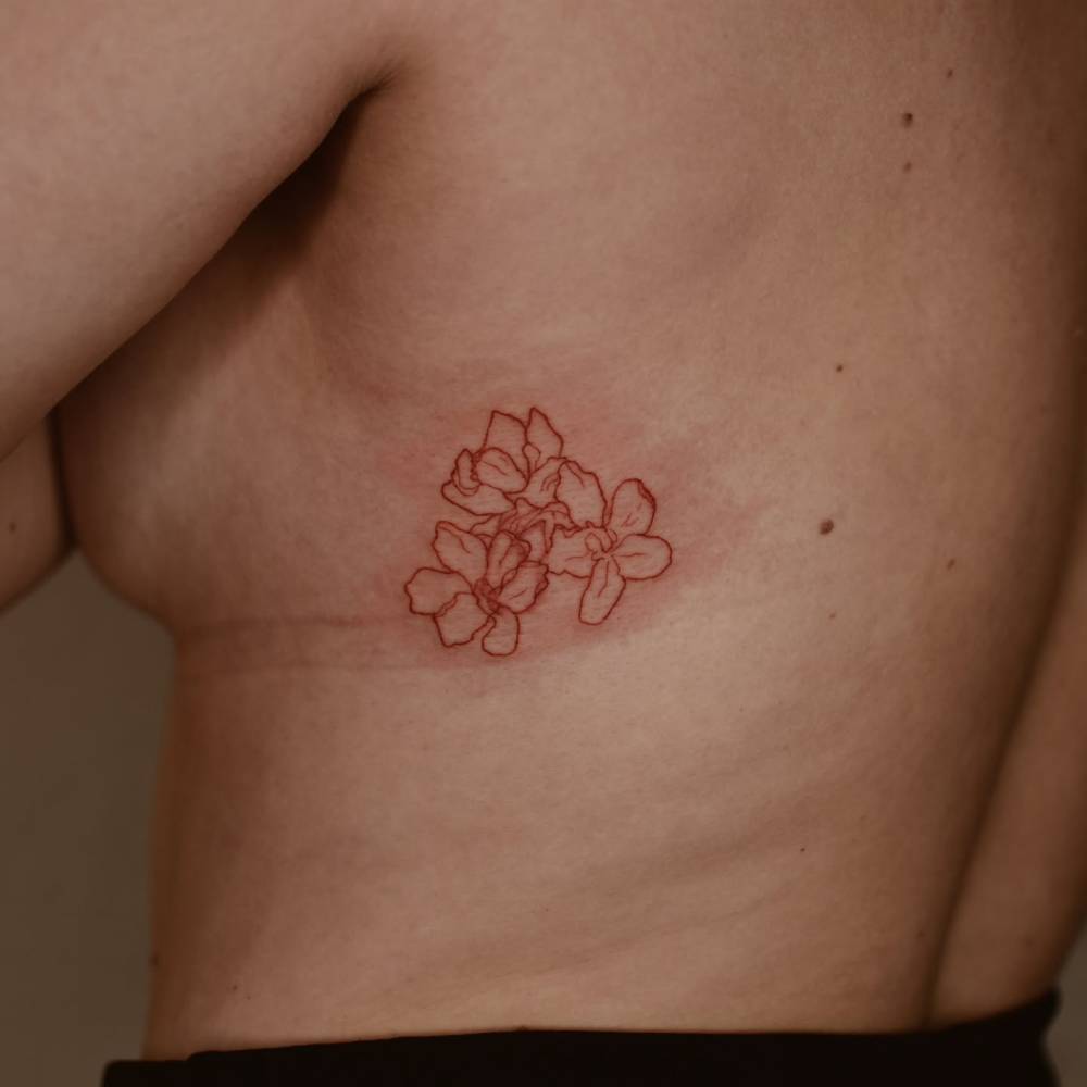 Red flowers tattoo in fine line style located on the side boob.