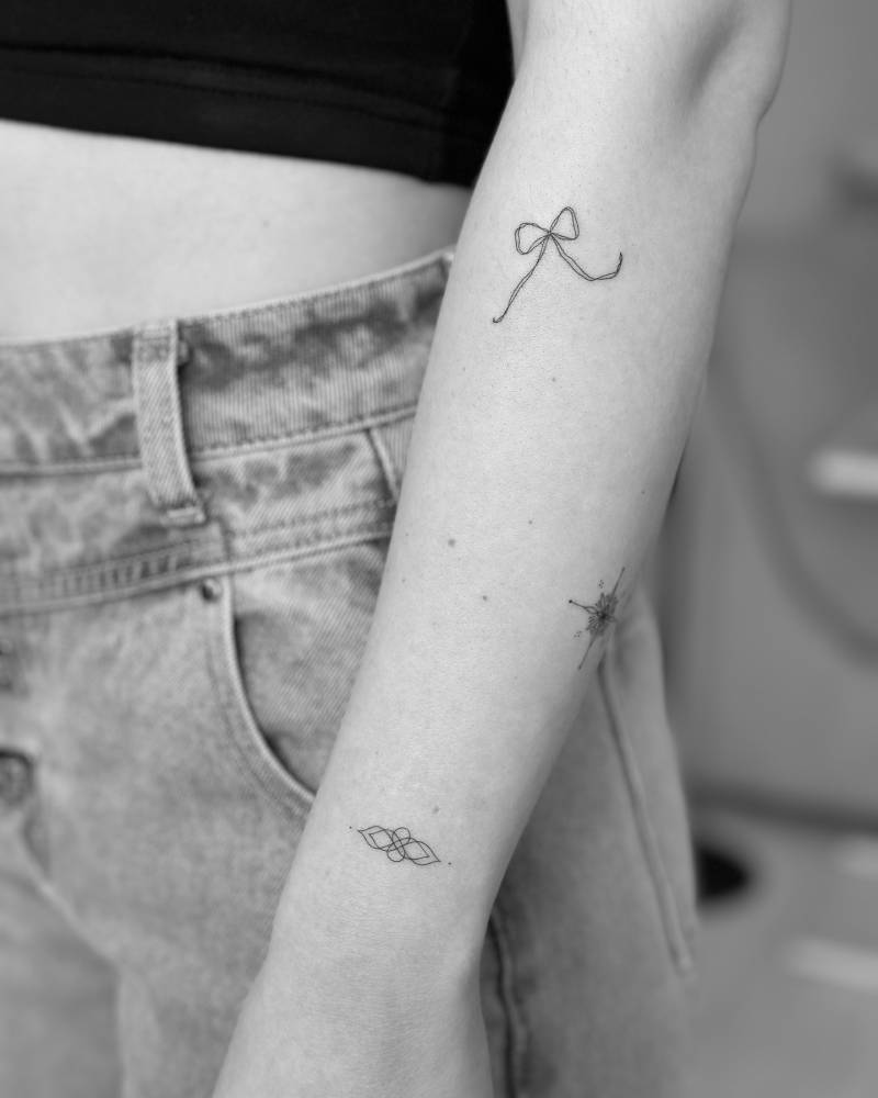 Fine line style ornament and bow tattoos located on the wrist and forearm.