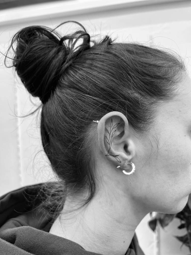 Leaves tattoo in fine line style located on the ear.
