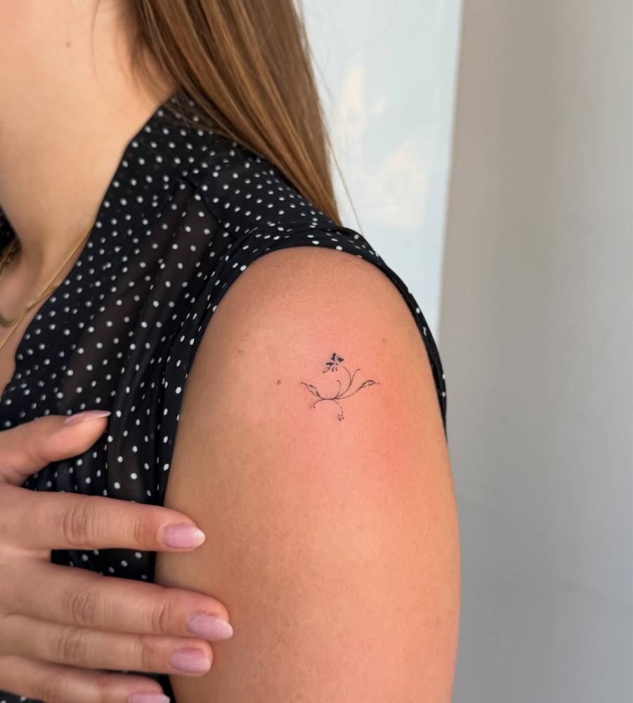 Little flower tattoo in fine line style located on the shoulder.